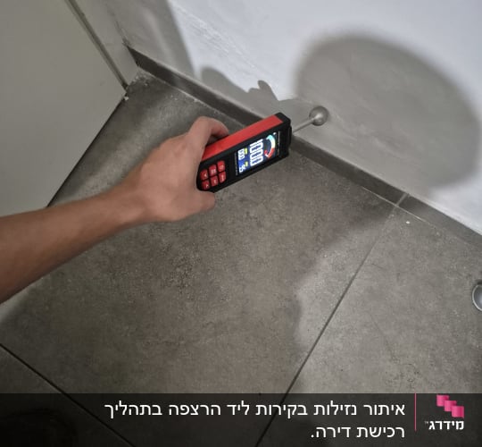 יד מחזיקה מכשיר מדידה על קיר ורצפה